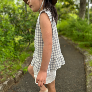 ギンガムチェック柄のノースリーブキッズトップスを着た女の子。muttaの夏の新作、涼しげなコットン素材とフリル裾が特徴