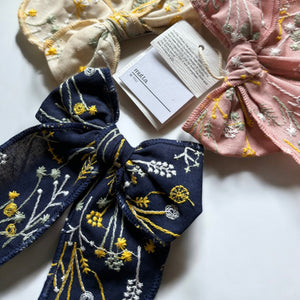 「刺繍入りのレトロシックなヘアリボン。ナチュラルカラーの生地にボタニカル柄の繊細な刺繍が施された、大きめサイズのリボンクリップ。ベビー&キッズ向けのおしゃれなヘアアクセサリー。