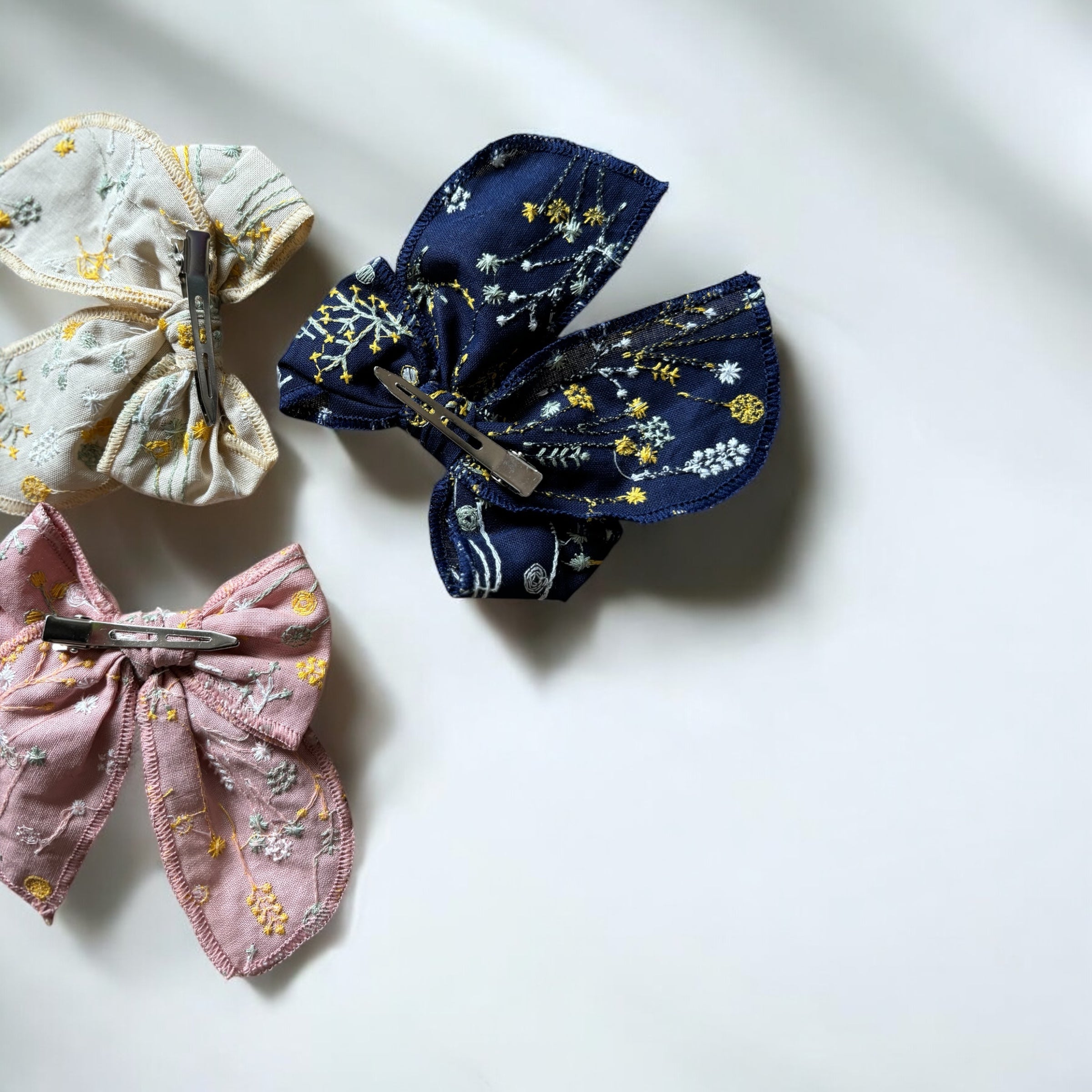 「刺繍入りのレトロシックなヘアリボン。ナチュラルカラーの生地にボタニカル柄の繊細な刺繍が施された、大きめサイズのリボンクリップ。ベビー&キッズ向けのおしゃれなヘアアクセサリー。