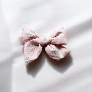 「小花柄が可愛い大きめサイズのヘアリボンクリップ。やさしいピンクカラーとナチュラルな風合いの生地が特徴で、ベビー&キッズ向けのおしゃれなヘアアクセサリー。簡単にヘアアレンジが楽しめるアイテム