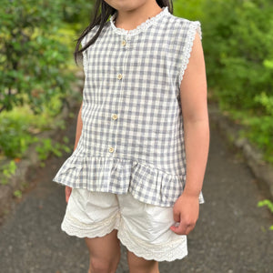 ギンガムチェック柄のノースリーブキッズトップスを着た女の子。muttaの夏の新作、涼しげなコットン素材とフリル裾が特徴