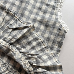 ギンガムチェック柄のノースリーブキッズトップスを着た女の子。muttaの夏の新作、涼しげなコットン素材とフリル裾が特徴