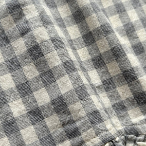 ギンガムチェック柄のノースリーブキッズトップスを着た女の子。muttaの夏の新作、涼しげなコットン素材とフリル裾が特徴