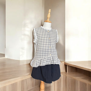 ギンガムチェック柄のノースリーブキッズトップスを着た女の子。muttaの夏の新作、涼しげなコットン素材とフリル裾が特徴