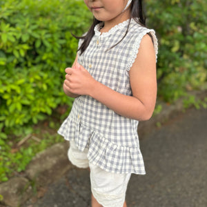ギンガムチェック柄のノースリーブキッズトップスを着た女の子。muttaの夏の新作、涼しげなコットン素材とフリル裾が特徴