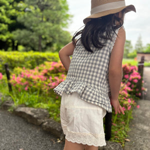 ギンガムチェック柄のノースリーブキッズトップスを着た女の子。muttaの夏の新作、涼しげなコットン素材とフリル裾が特徴