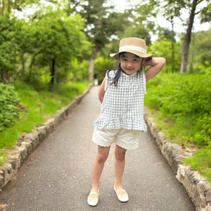 ギンガムチェック柄のノースリーブキッズトップスを着た女の子。muttaの夏の新作、涼しげなコットン素材とフリル裾が特徴