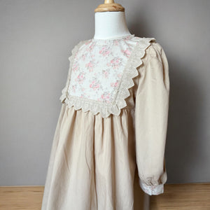 ベージュのクラシカルワンピースを着る女の子。胸元に小花柄とレースが施され、秋冬のお出かけや家族写真にぴったりの子供服