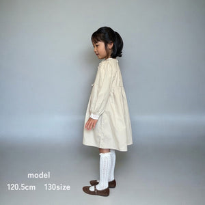 ベージュのクラシカルワンピースを着る女の子。胸元に小花柄とレースが施され、秋冬のお出かけや家族写真にぴったりの子供服