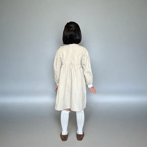 ベージュのクラシカルワンピースを着る女の子。胸元に小花柄とレースが施され、秋冬のお出かけや家族写真にぴったりの子供服