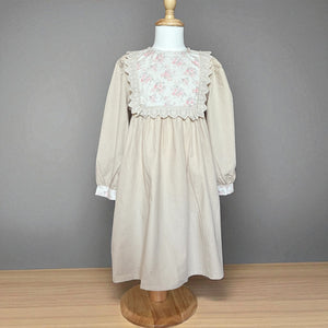 ベージュのクラシカルワンピースを着る女の子。胸元に小花柄とレースが施され、秋冬のお出かけや家族写真にぴったりの子供服