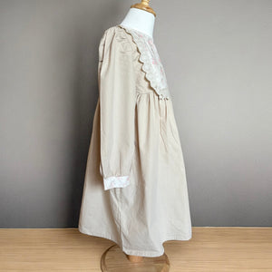 ベージュのクラシカルワンピースを着る女の子。胸元に小花柄とレースが施され、秋冬のお出かけや家族写真にぴったりの子供服