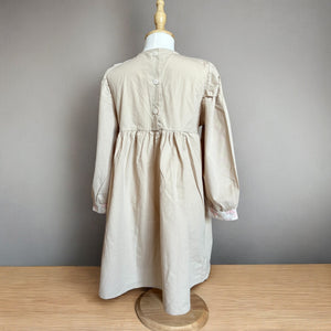 ベージュのクラシカルワンピースを着る女の子。胸元に小花柄とレースが施され、秋冬のお出かけや家族写真にぴったりの子供服