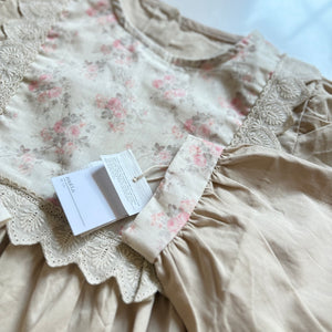 ベージュのクラシカルワンピースを着る女の子。胸元に小花柄とレースが施され、秋冬のお出かけや家族写真にぴったりの子供服