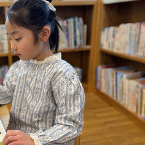 ブルーの小花柄ストライプブラウスと、オフホワイトのパンツの子供向けセットアップ。フリルの襟と袖口が可愛らしいストライプデザイン