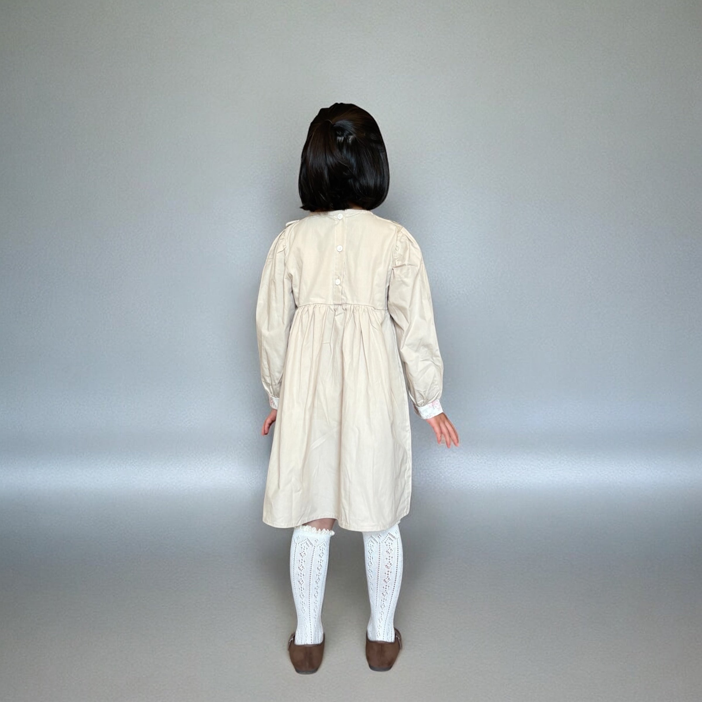 ベージュのクラシカルワンピースを着る女の子。胸元に小花柄とレースが施され、秋冬のお出かけや家族写真にぴったりの子供服